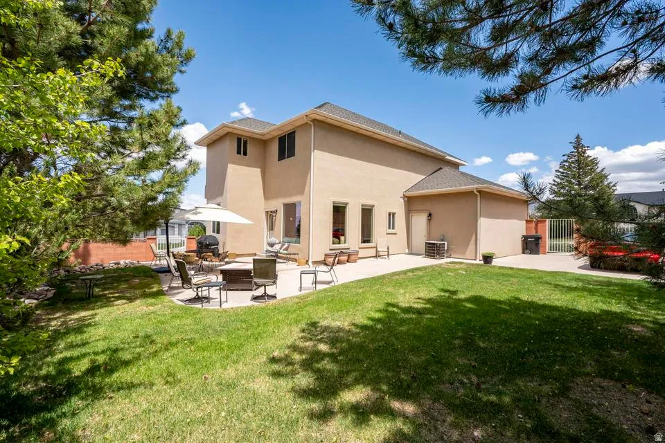 Expansive backyard featuring a manicured lawn, a large concrete patio, and a stucco exterior