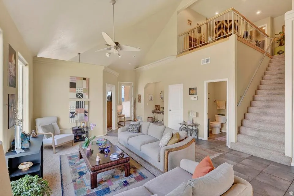 Spacious living area featuring vaulted ceilings with a ceiling fan, a carpeted staircase leading to an upper-level landing with metal railing, and tile flooring