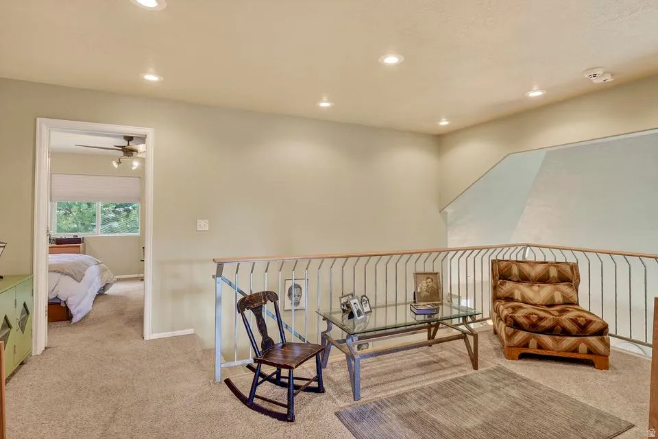 Carpeted loft space featuring a metal railing and recessed lighting