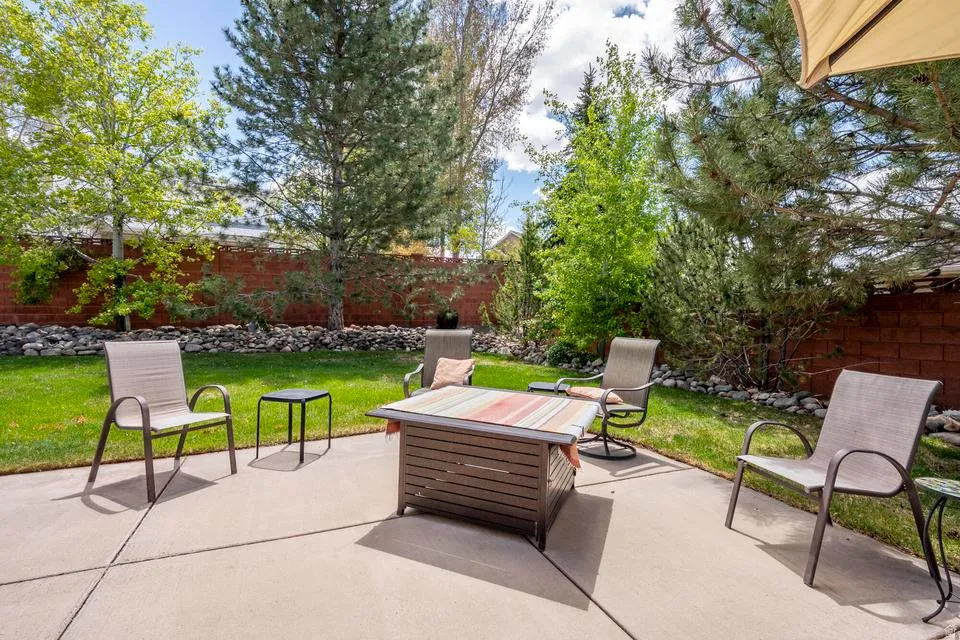 Concrete patio with a fire pit feature, surrounded by a grassy lawn and mature trees