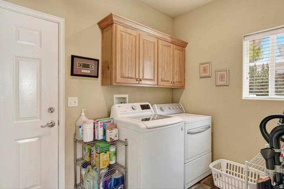 Dedicated utility space featuring overhead wood-finish cabinetry, a white paneled door with brushed nickel hardware, and a window with horizontal blinds