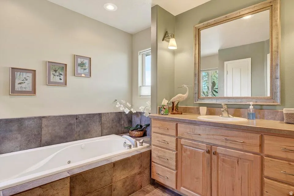 Spacious bathroom featuring a built-in soaking tub, a large vanity with ample storage, a framed mirror, and a window with privacy blinds