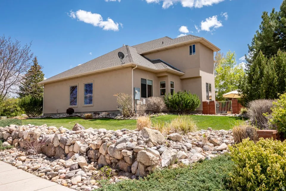Exterior stucco home featuring a stone retaining wall, mature landscaping, a manicured lawn, and a private patio with a white metal gate