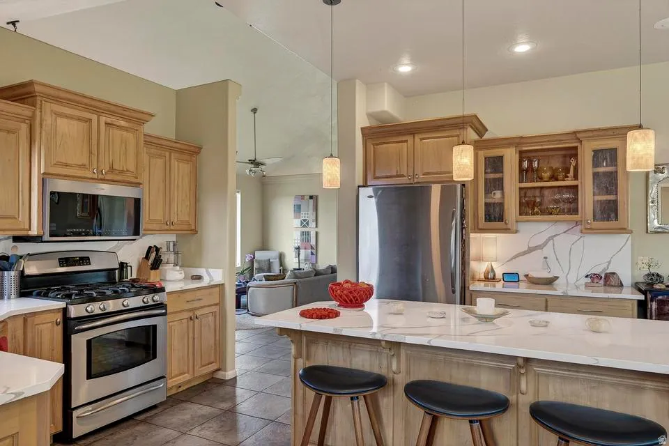 Spacious kitchen featuring light wood cabinetry, stainless steel appliances, a large island with seating, and a white countertop with prominent veining