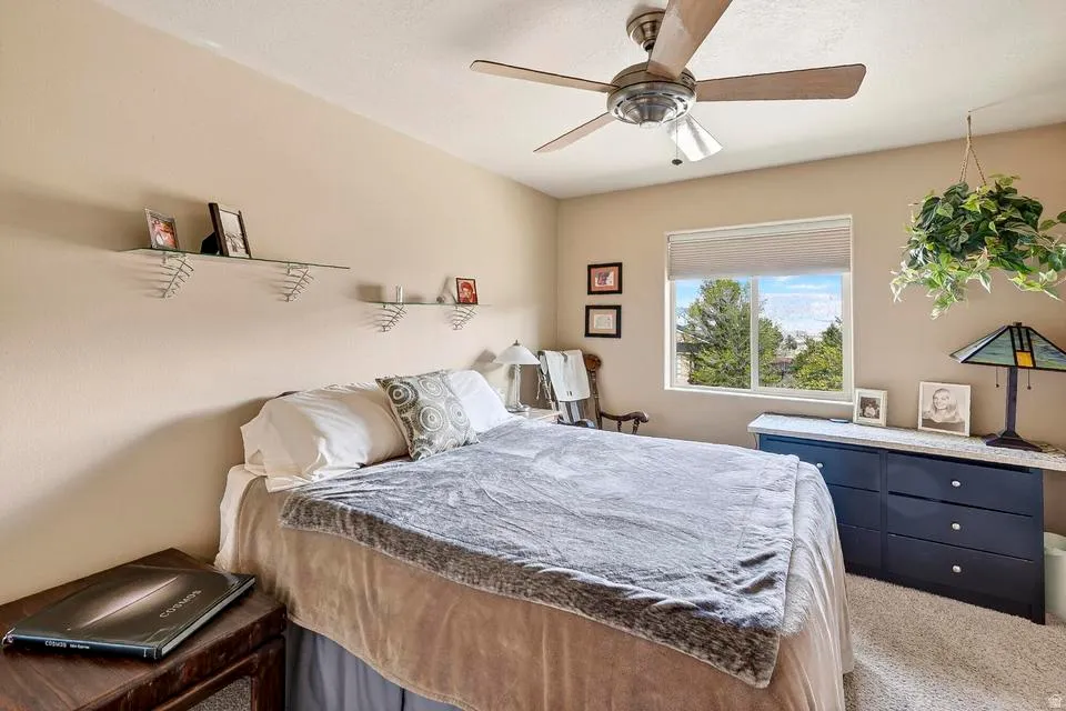 Carpeted bedroom featuring a large window, ceiling fan with light fixture, and built-in shelving