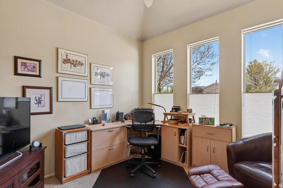 Vaulted ceiling room featuring three tall windows with privacy blinds, built-in corner desk cabinetry, and neutral wall tones
