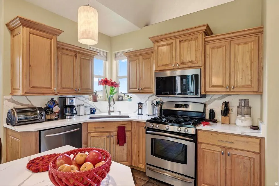 Kitchen featuring wood-finish cabinetry, stainless steel appliances, white countertops, and a white backsplash with gray veining