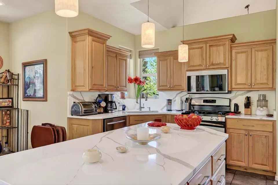 Gourmet kitchen featuring a large central island with a white veined countertop, stainless steel appliances, abundant wood cabinetry, and pendant lighting