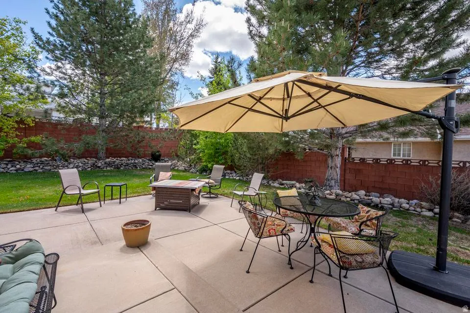 Expansive concrete patio with a detached umbrella, surrounded by a manicured lawn and mature trees