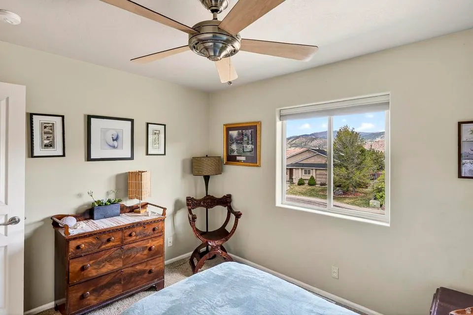 Light-filled room featuring a ceiling fan with wood-finish blades, a sliding window with roller shades, and views of distant hills