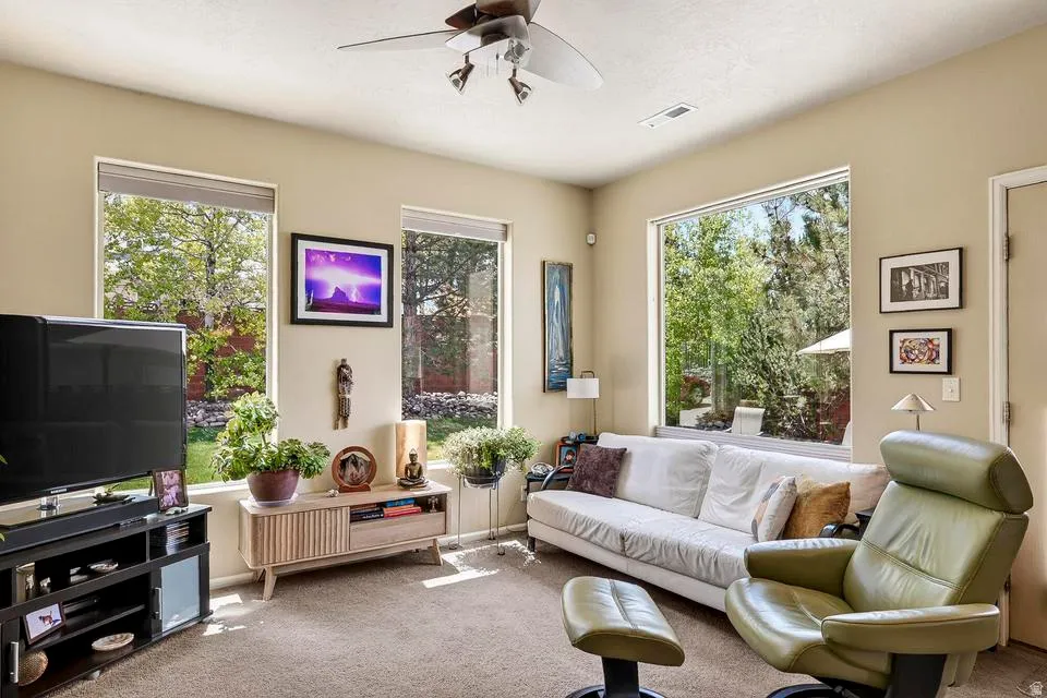 Living area featuring multiple large windows, neutral-toned walls, and a ceiling fan