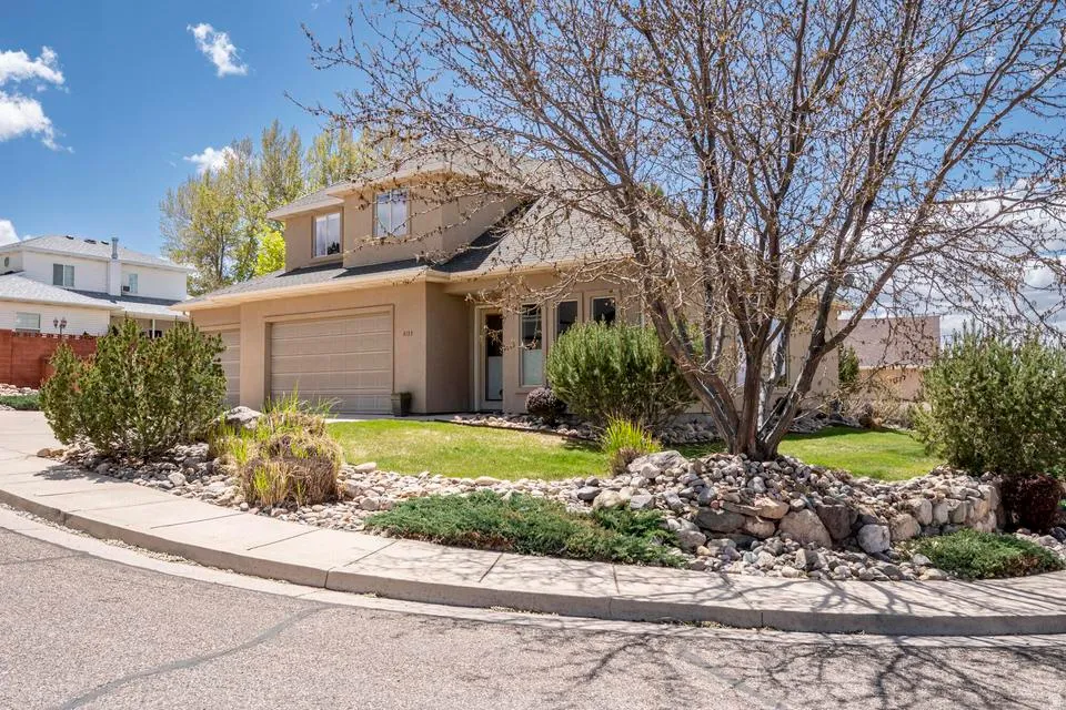 Two-story stucco residence with a two-car garage, featuring a mature tree and established landscaping with rock accents