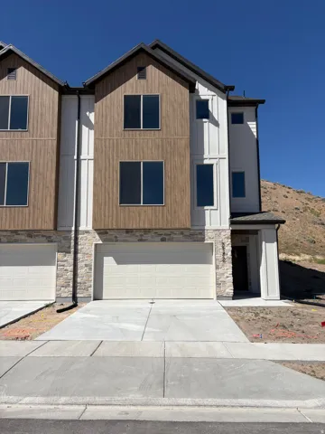 Contemporary townhome exterior featuring a two-car garage, stone facade, vertical wood-finish siding, white board and batten accents, and dark-framed windows