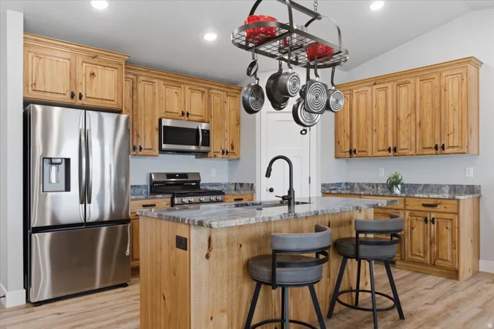 Kitchen featuring a central island with a built-in sink and seating space, wood-finish cabinetry, stainless steel appliances, and light-colored flooring
