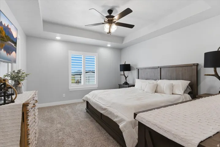 Spacious room featuring a tray ceiling with recessed lighting, a ceiling fan with integrated light, a window with plantation shutters, and light-toned carpet flooring