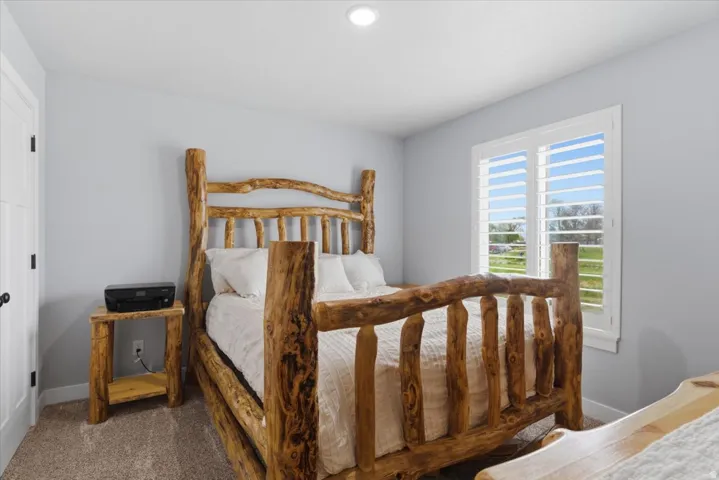 Spacious room with plush carpeting, light gray wall tones, and a bright window featuring plantation shutters