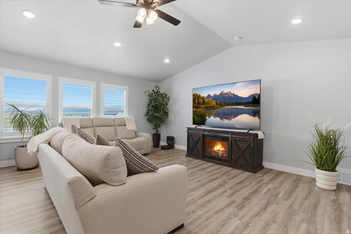 Spacious living area featuring vaulted ceilings with recessed lighting, wood-finish flooring, and multiple windows