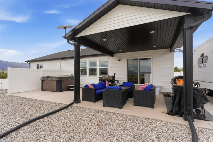 Expansive concrete patio featuring a covered outdoor living area with recessed lighting, a sliding glass door, a hot tub, and a white privacy fence