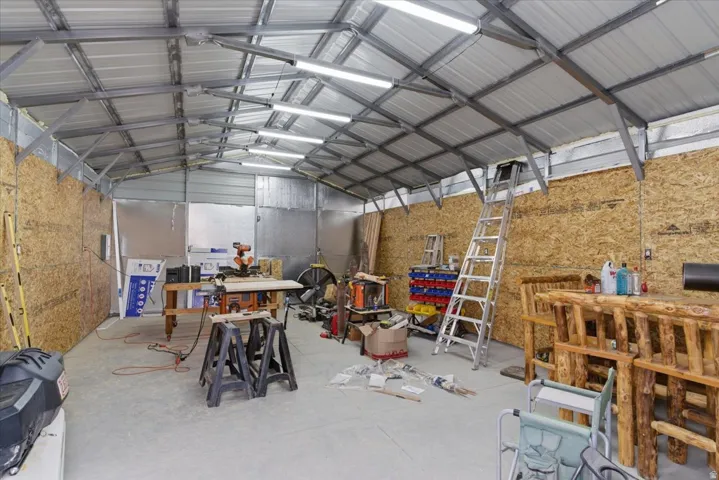 Spacious utility building featuring a metal roof, exposed metal beam ceiling, fluorescent lighting, and oriented strand board walls
