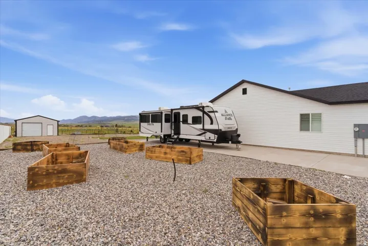 Spacious gravel yard featuring multiple raised garden beds, a concrete driveway, and a white siding structure with a dark roof
