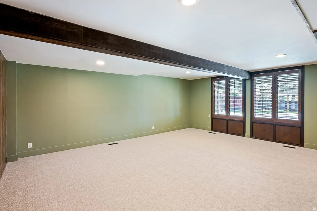 Spacious interior room featuring light-colored carpeting, recessed lighting, and exposed dark wood beams