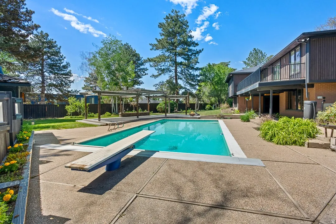 Expansive outdoor living area featuring a rectangular swimming pool with diving board, a surrounding concrete patio, and a pergola structure