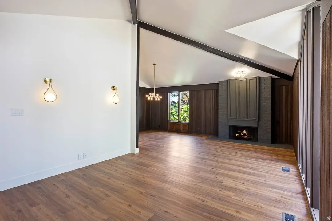 Spacious interior featuring wood-finish flooring, a contemporary fireplace with a paneled surround, and a vaulted ceiling with exposed beams