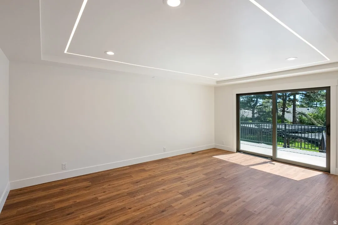 Spacious room featuring wood-finish flooring, white walls, and a recessed ceiling with integrated lighting