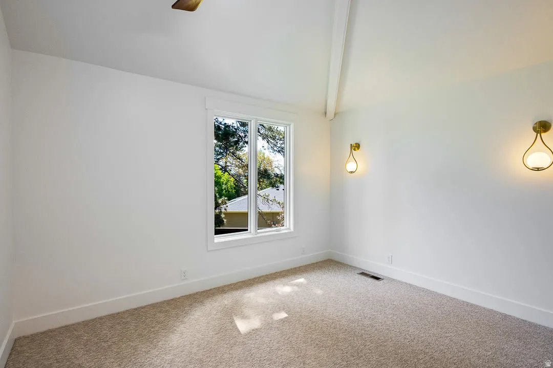 Room featuring vaulted ceilings with exposed beams, two wall-mounted sconces, a large window, and carpet flooring