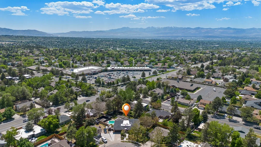 Aerial perspective showcasing a residential area with mature trees, a commercial center, and distant mountains