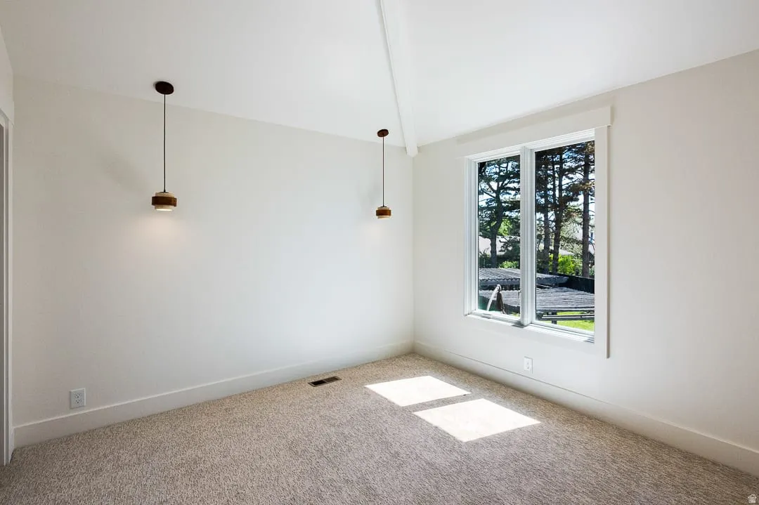 Vaulted ceiling room featuring a large window, neutral wall paint, plush carpeting, and two contemporary pendant lights with wood-finish accents