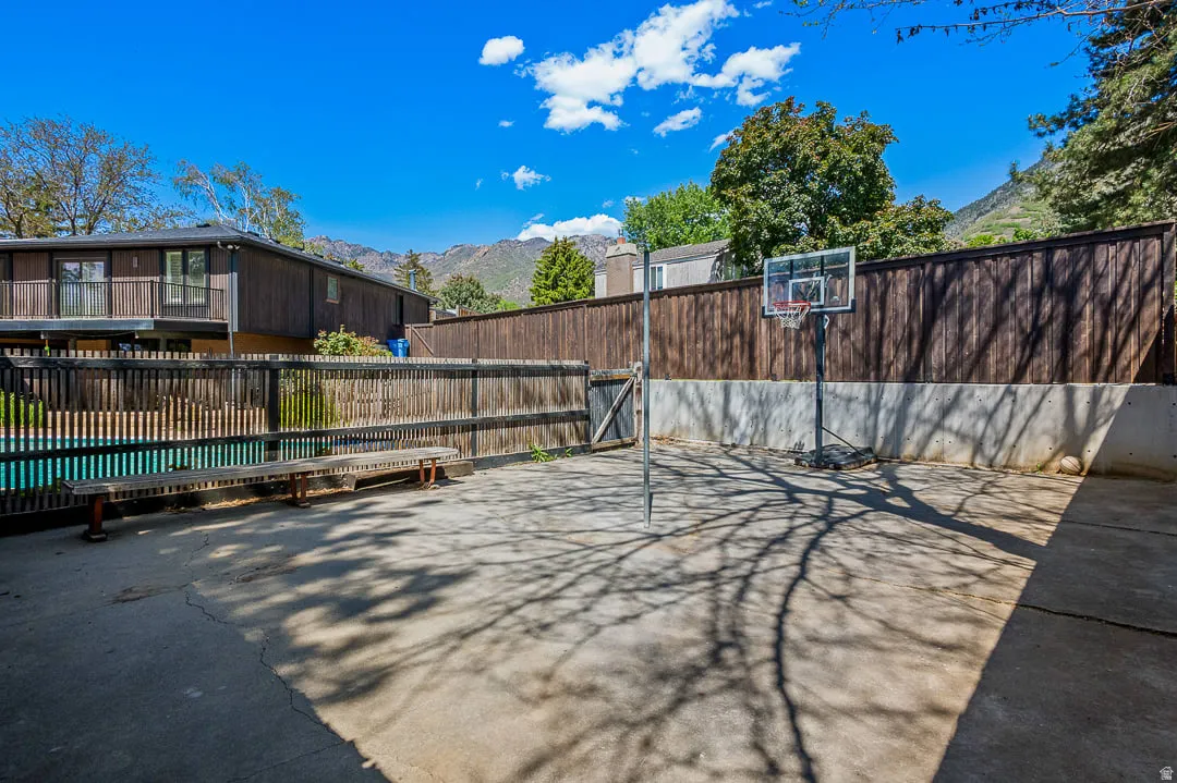 Concrete patio featuring a privacy fence, an adjacent swimming pool, and a mountain backdrop