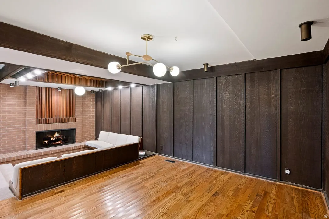 Hardwood flooring throughout featuring a spacious living area with a brick fireplace, wood paneling, and built-in bench seating