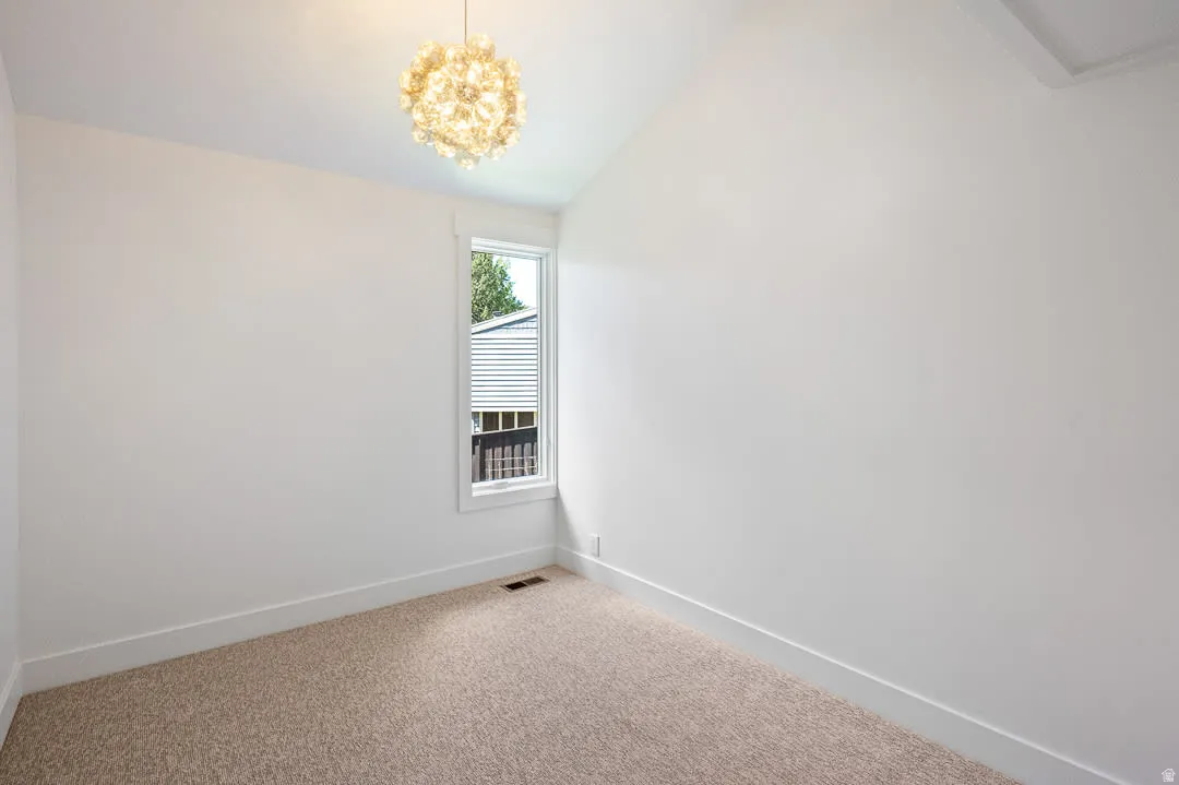 Vaulted ceiling room featuring a contemporary light fixture, single window, clean white walls, and neutral-toned carpeting
