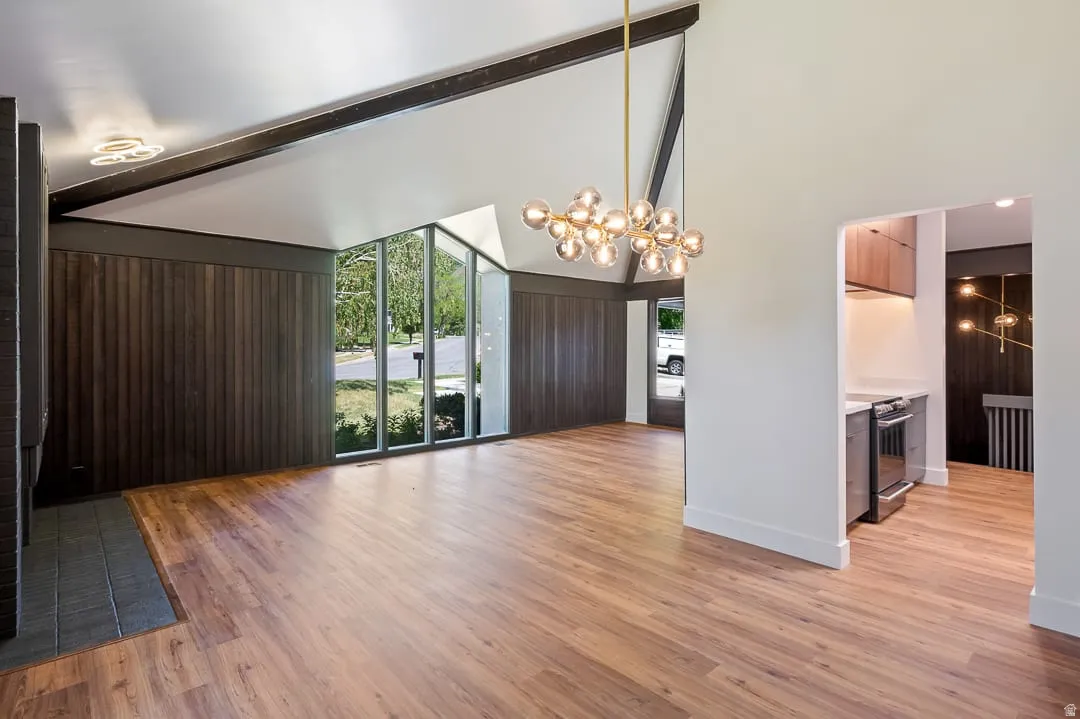 Vaulted ceiling with exposed beams, wood-finish flooring, full-height windows, and a modern chandelier