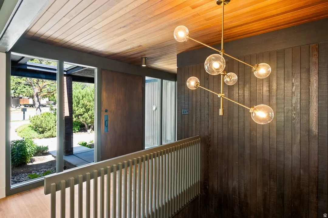 Entryway featuring a wood-panel ceiling, dark wood-paneled wall, and a modern brass chandelier