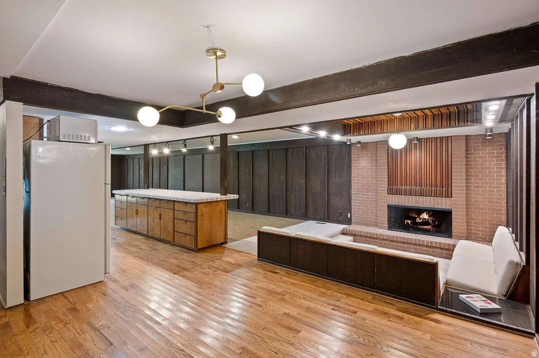 Hardwood flooring extends throughout this expansive space, featuring a large central island with ample storage, a brick-surround fireplace, and recessed built-in seating