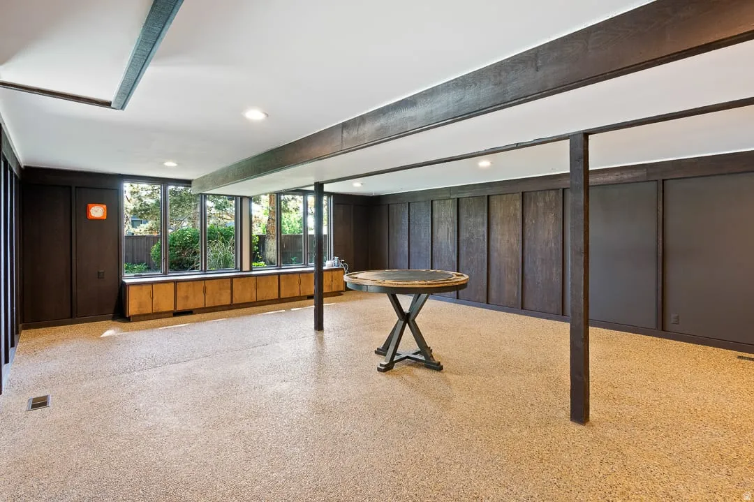 Spacious room featuring a wall of floor-to-ceiling windows, dark wood paneling, wood-finish beams, recessed lighting, and built-in wood-finish cabinetry