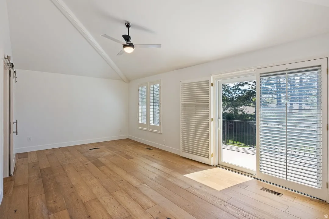 Spacious interior featuring wood-finish flooring, a vaulted ceiling with exposed beam, and a modern ceiling fan