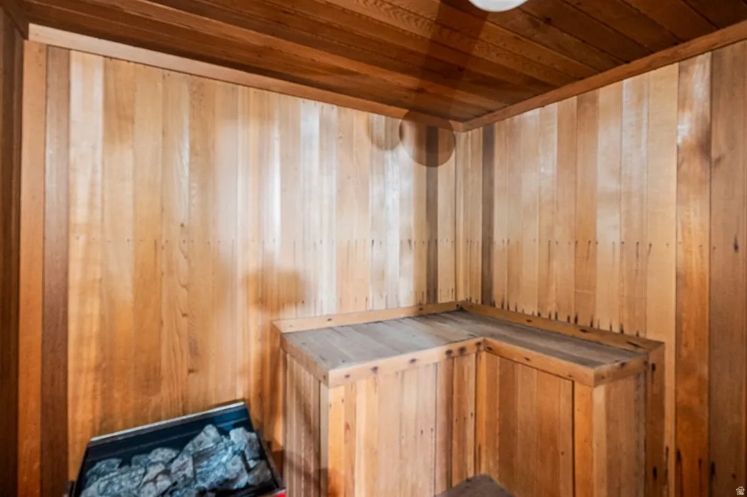 Sauna interior featuring wood paneling, wood-plank ceiling, built-in L-shaped bench, and a rock heater