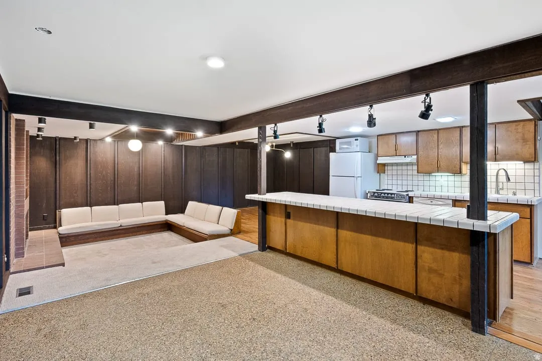 Open-concept lower level featuring a built-in seating area, a fireplace with a brick surround, and an integrated kitchen space