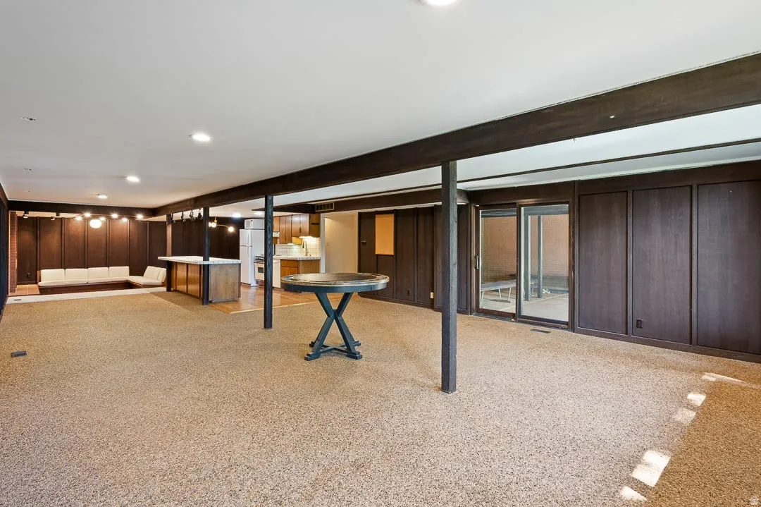 Spacious lower-level room featuring textured wood-paneling walls, exposed dark wood beams, and recessed lighting