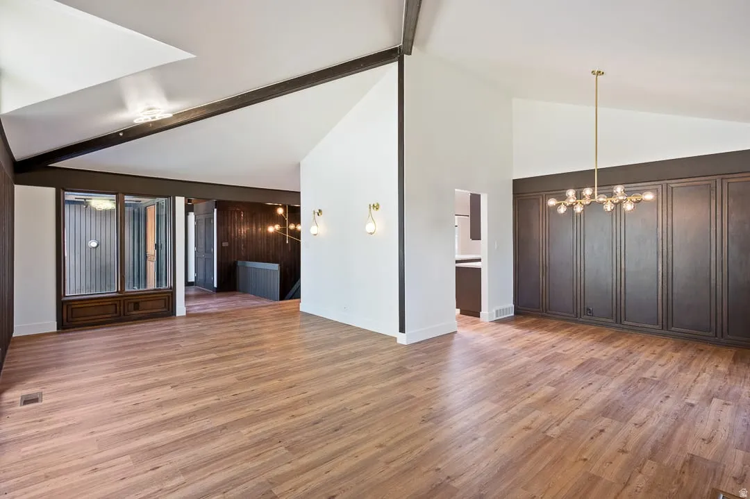 Spacious open-concept room featuring vaulted ceilings, wood-finish flooring, a contemporary linear chandelier, and integrated wall paneling