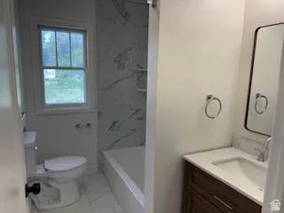 Bathroom featuring a wood-finish vanity with an integrated sink and light-toned countertop, a framed mirror, and a tiled tub surround