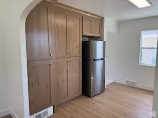 Integrated wood-finish cabinetry and stainless steel refrigerator with wood-finish flooring, white baseboards, and a window