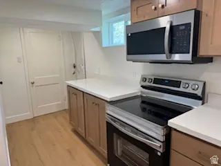 Kitchen area featuring a stainless steel microwave and electric range, light wood-finish cabinetry, light-toned countertops, and wood-finish flooring