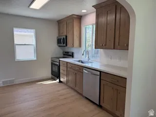 Kitchen featuring wood-finish cabinetry, stainless steel appliances, a single basin sink with a gooseneck faucet, light-toned countertops, and wood-finish flooring