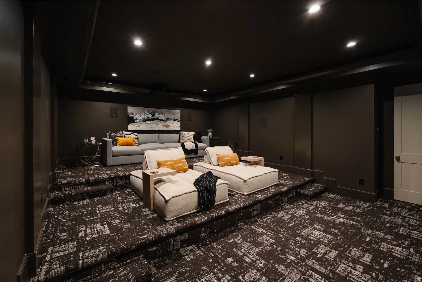 Tiered entertainment room featuring dark walls, recessed ceiling lighting, textured wall-to-wall carpeting, and a white paneled door