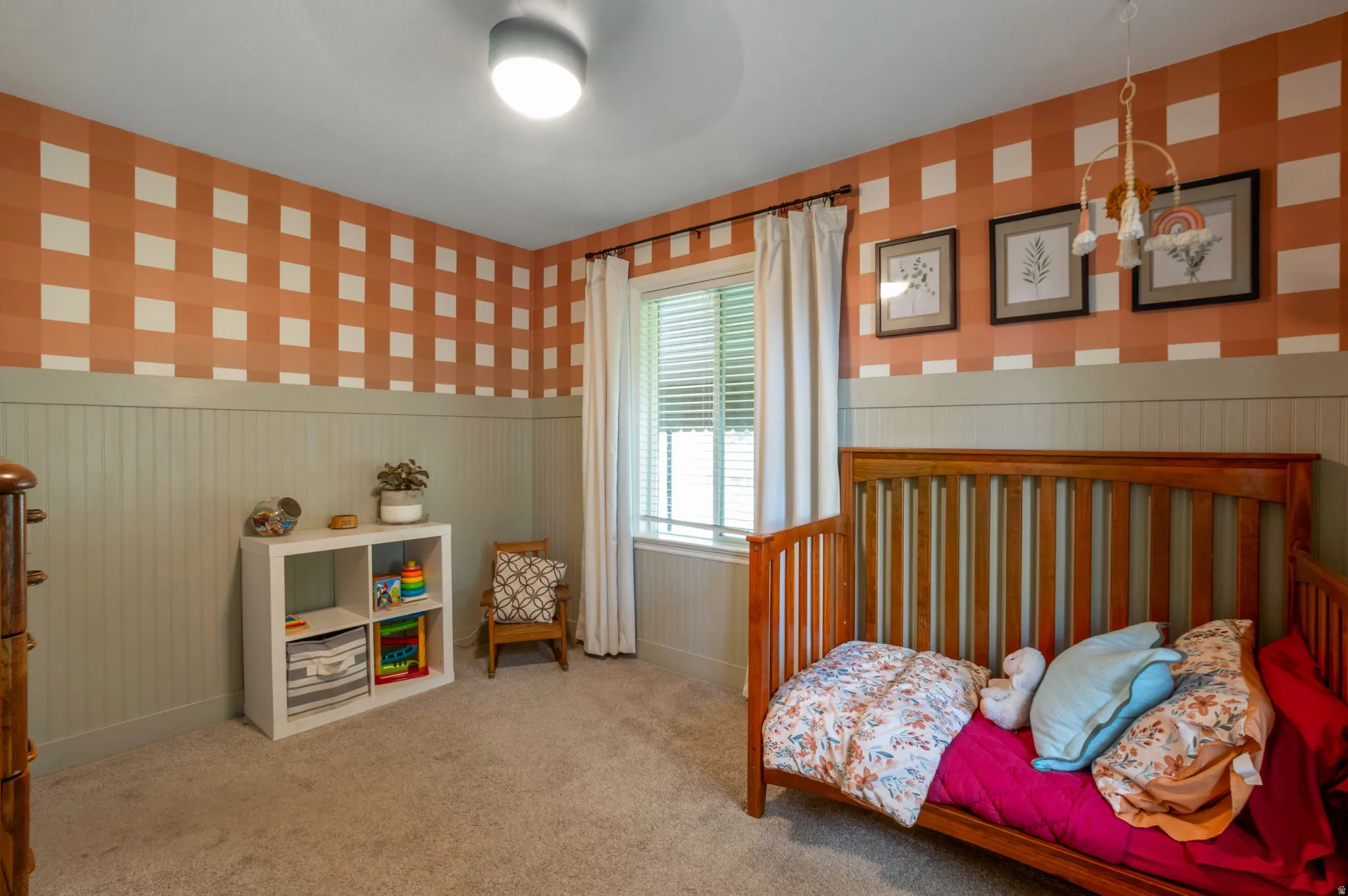 Carpeted room featuring board and batten wainscoting, an accent wall with a checkered pattern, and a window with blinds