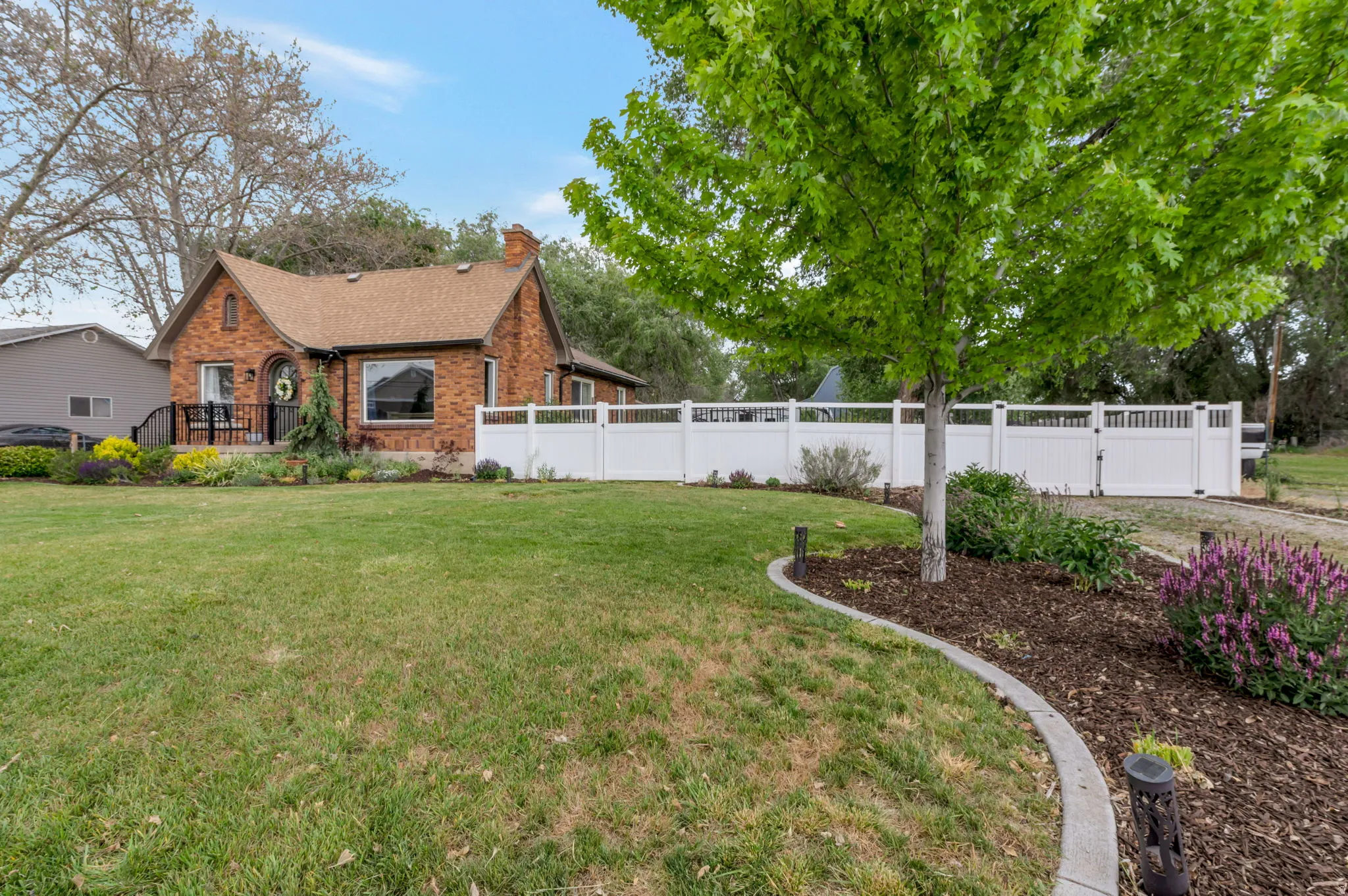 Brick exterior residence featuring a front porch, white fence, and mature landscaping